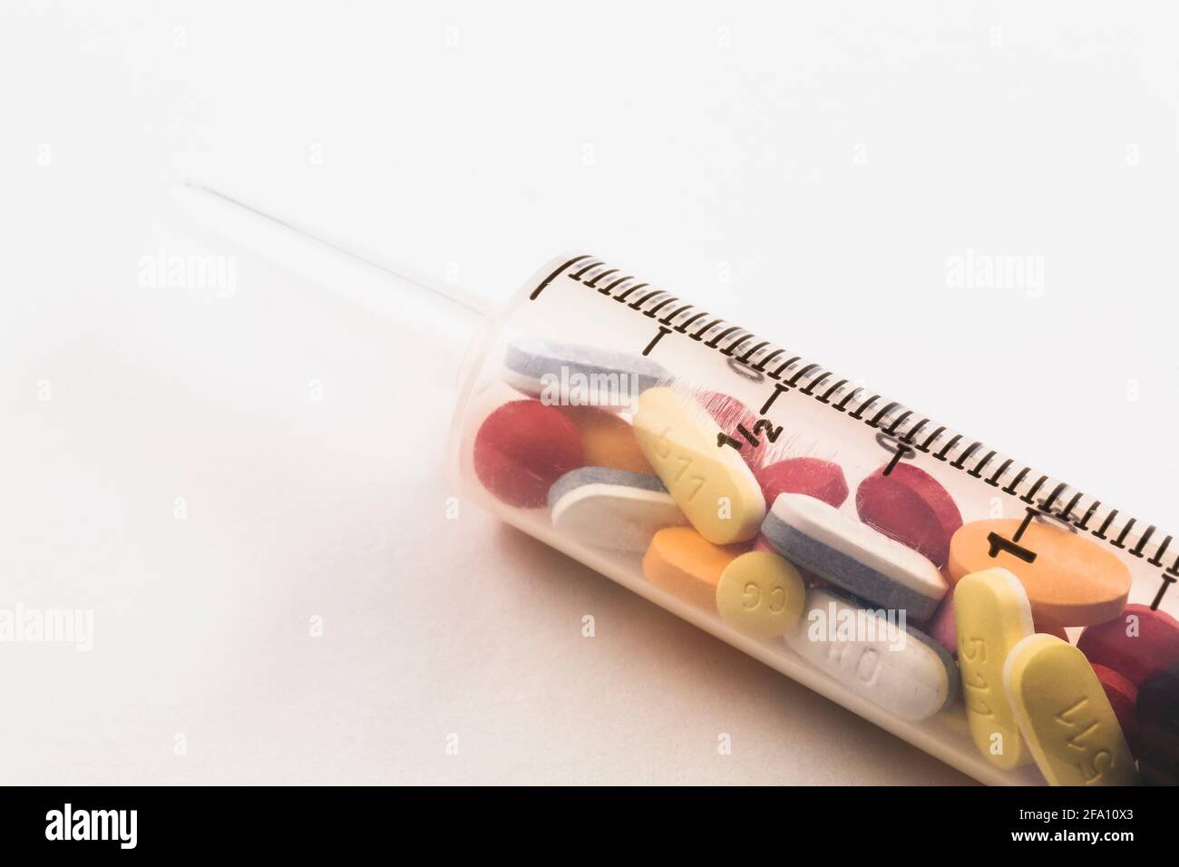 Siringa riempita con pillole di medicina assortite su sfondo bianco Foto Stock