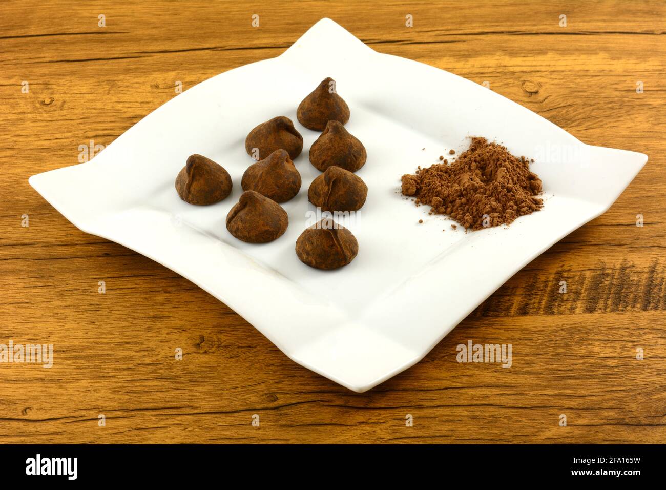 Tartufi al cioccolato polverizzati al cacao con cacao in polvere su spuntino bianco piastra sul tavolo Foto Stock