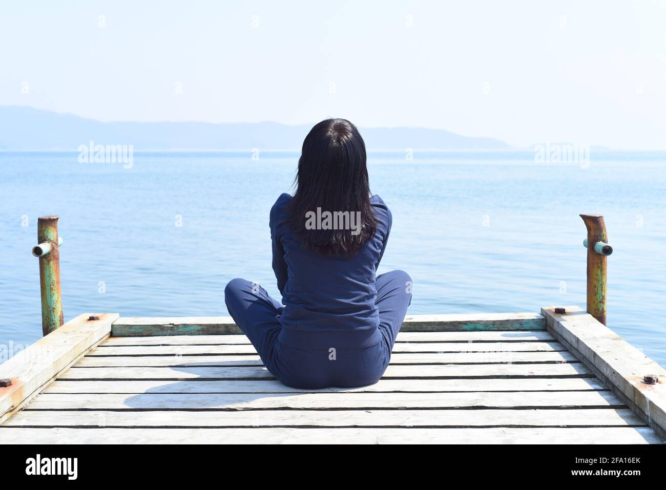 45 anni Donna russa seduta in posizione loto su un molo di legno contro il mare giapponese Foto Stock