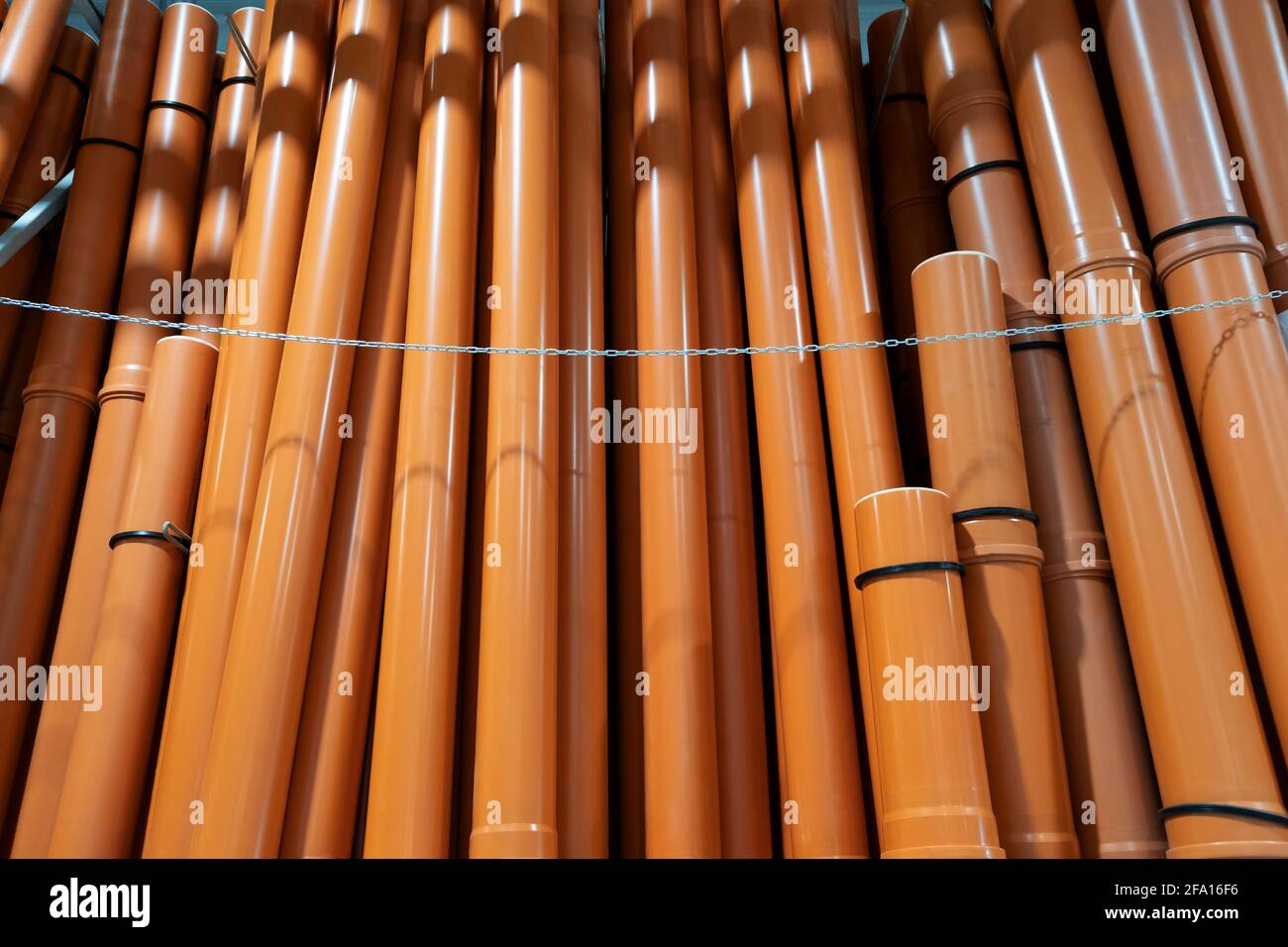 Pila di tubi di canalizzazione U in PVC su un magazzino di ferramenta. Disposti su un mucchio di tubi di plastica marrone. Industriale per tubi idraulici per cantieri esterni. Con Foto Stock