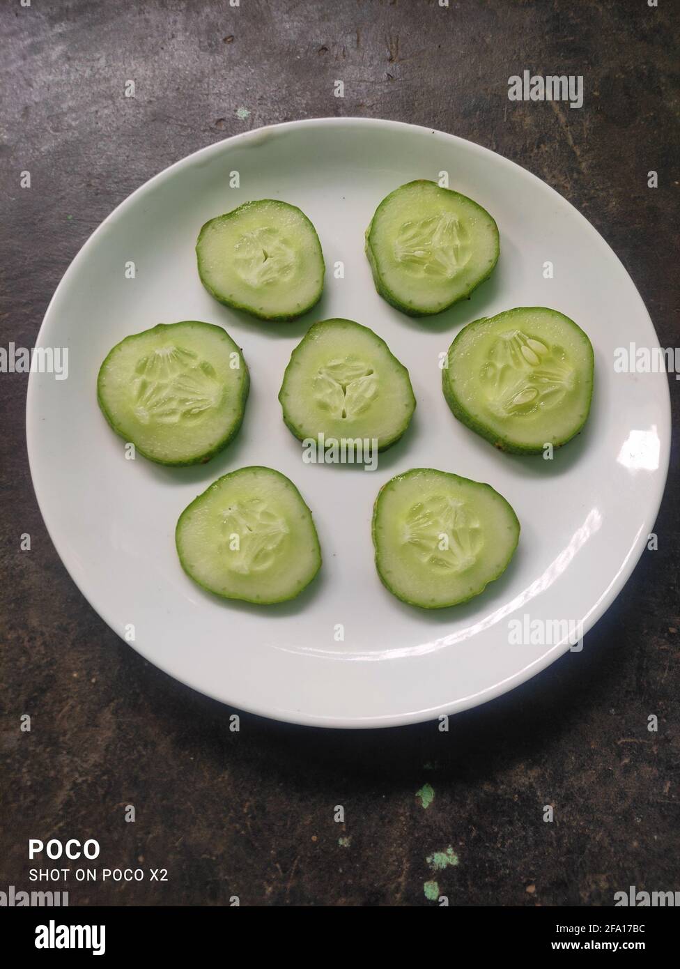 Un piatto di fette di cetriolo fresche e sane che vengono affettate con il coltello Foto Stock