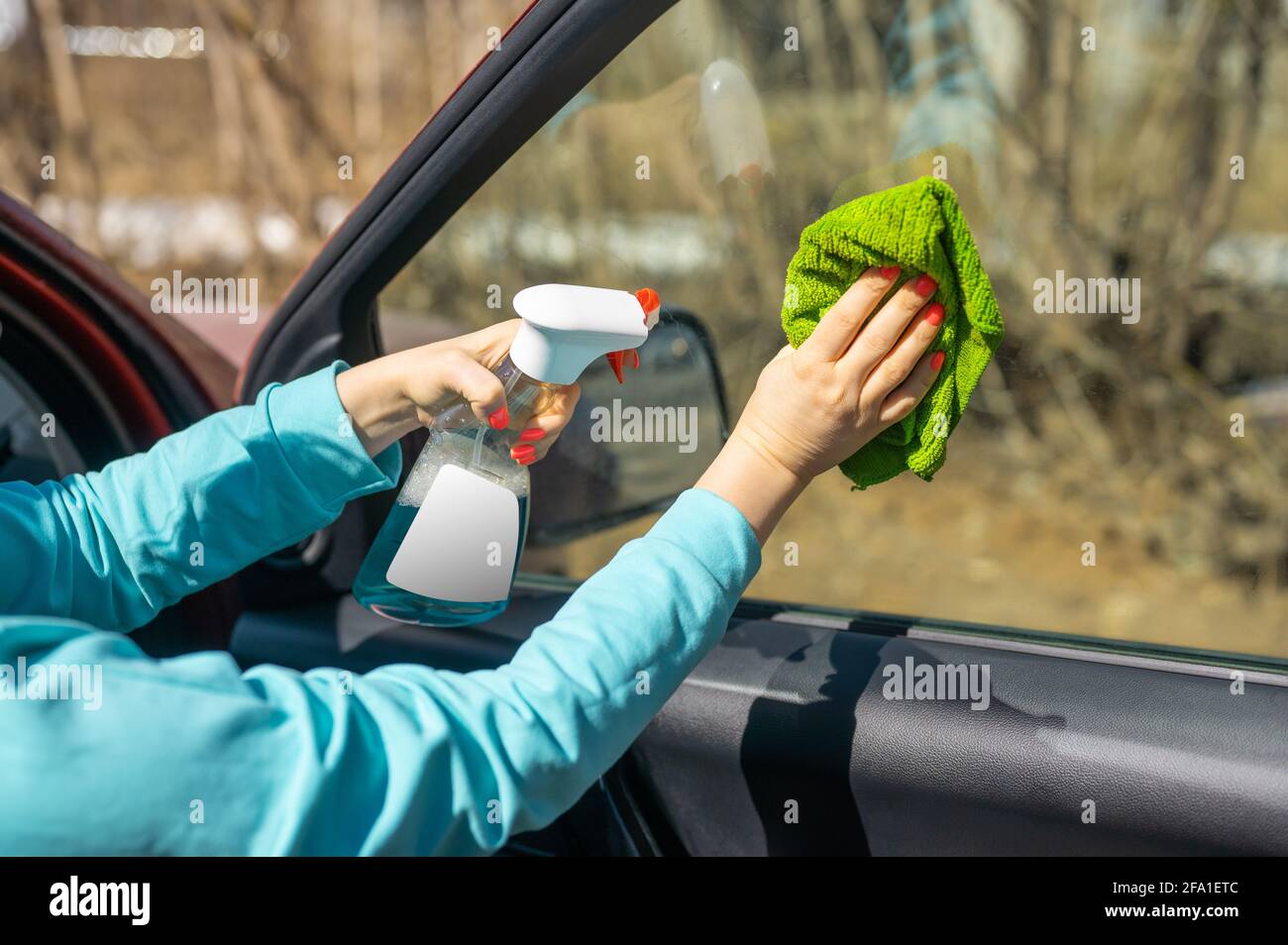 pulizia dei finestrini dell'auto. mani femminili pulizia dei finestrini dell'auto con panno in microfibra verde e flacone spray con etichetta bianca vuota per il tuo disegno. spazio per la copia Foto Stock