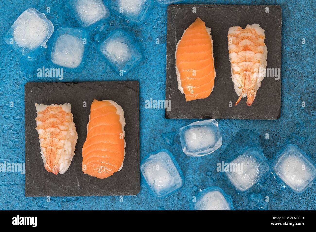 Vista dall'alto di due piatti d'ardesia con nigiri sushi e. cubetti di ghiaccio su sfondo blu Foto Stock