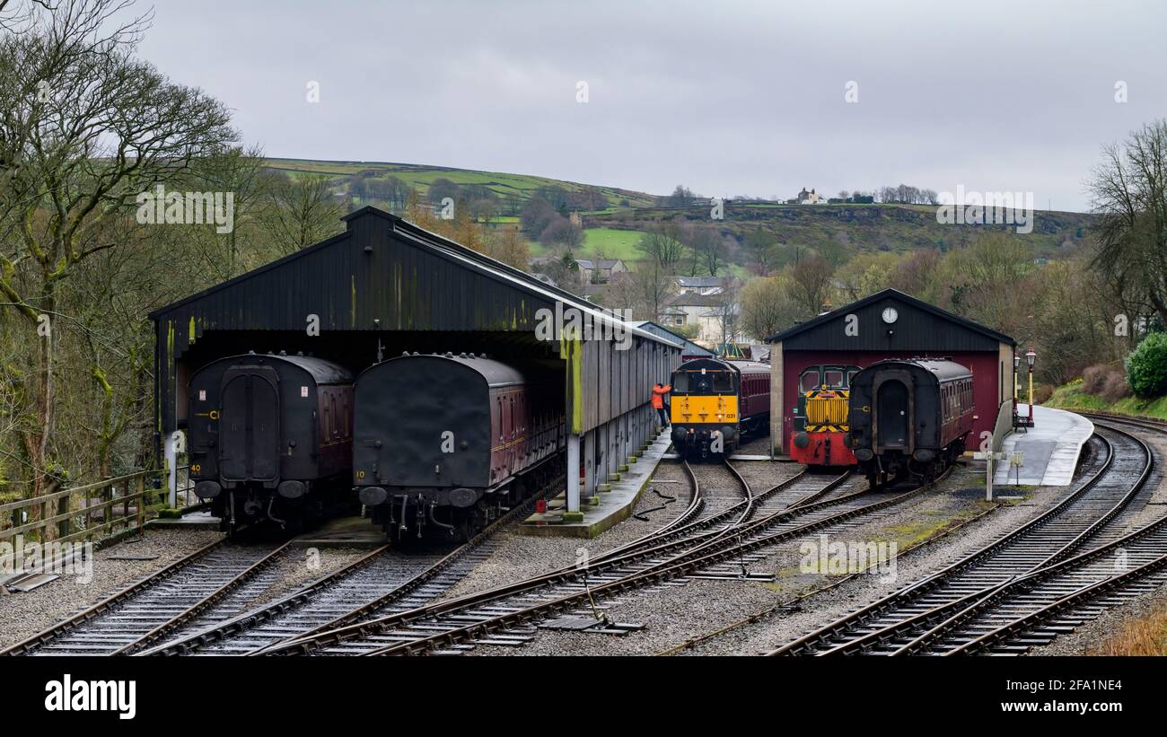 Storico treno diesel o loco, operaio ferroviario arrampicata da cabina, pullman vintage in capannoni motore) - Oxenhope Station sidings, Yorkshire, Inghilterra, Regno Unito. Foto Stock