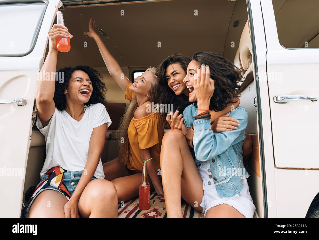 Gruppo multietnico di donne che si aggirano durante il viaggio. Amici in van alzando le mani e ridendo. Foto Stock