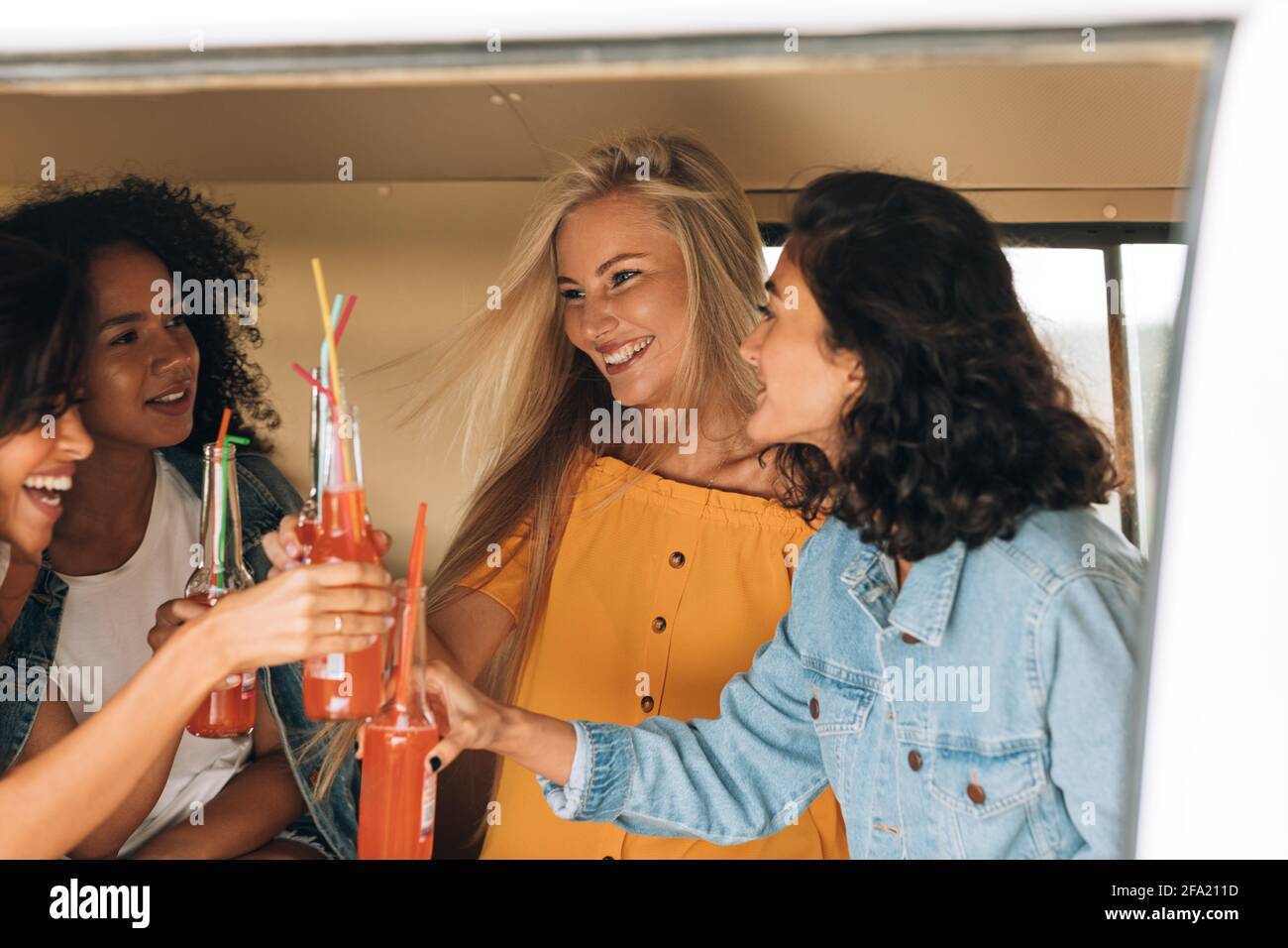 Quattro donne che tostano con bottiglie mentre si siedono in camper Foto Stock