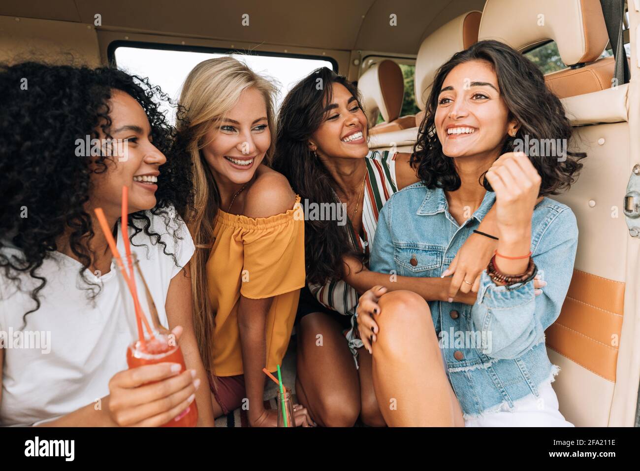 Donne sorridenti che si siedono insieme in pulmino godendo la vacanza estiva. Belle donne in viaggio. Foto Stock