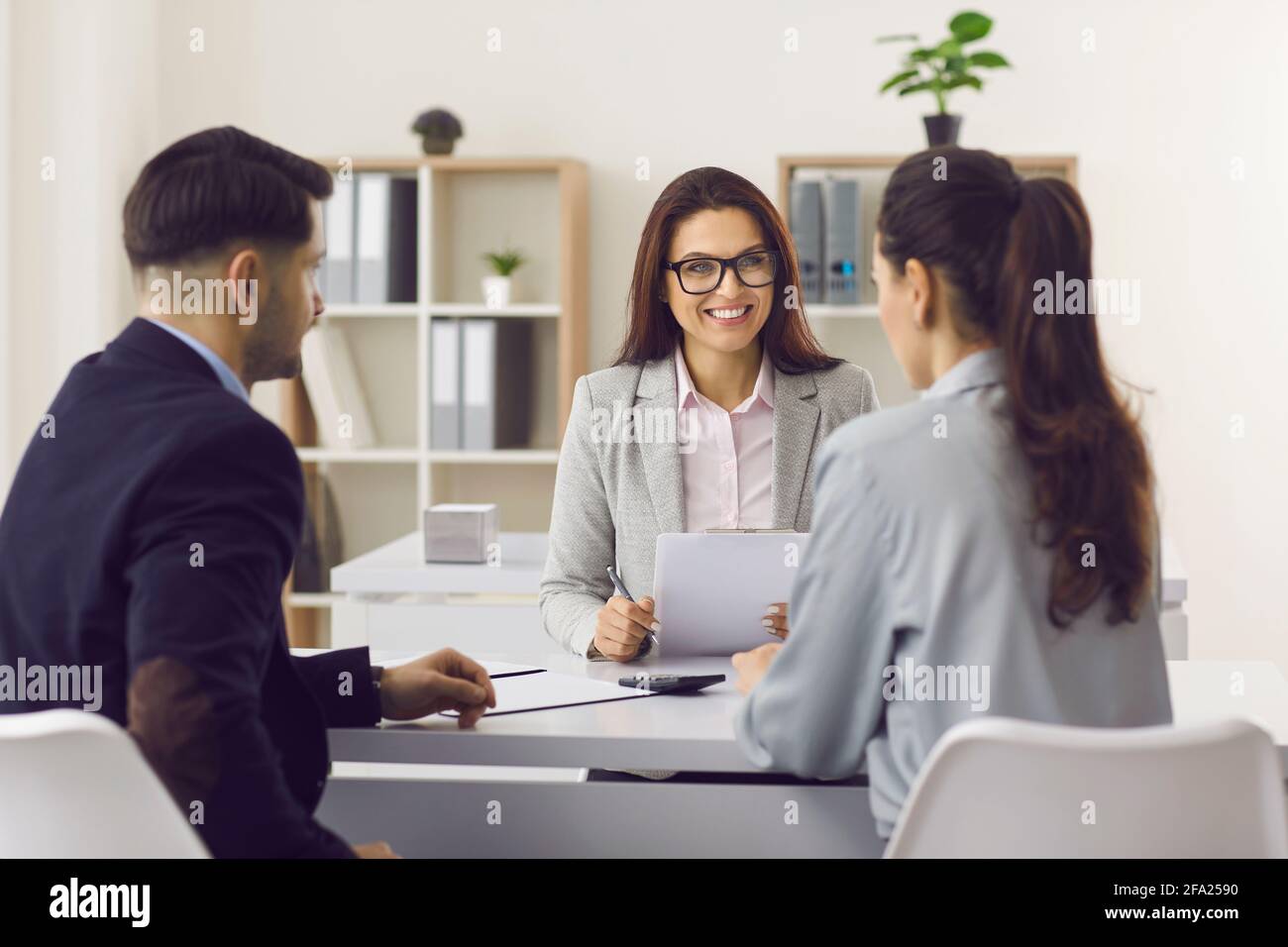 Amichevole manager di assicurazione o prestito broker incontro con giovane coppia nel suo ufficio Foto Stock