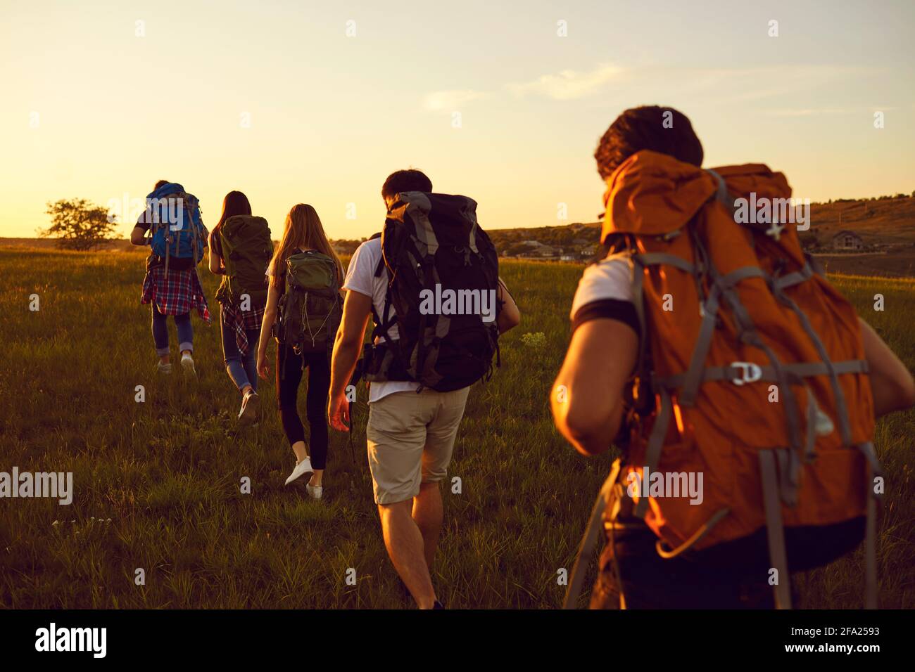 Gruppo di viaggiatori con zaini che camminano in file singolo in il campo durante le vacanze estive attive Foto Stock