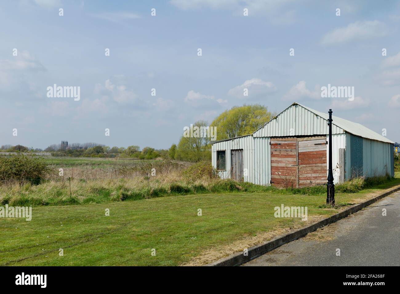 Derelict corrugato costruzione fiancheggiante terreni agricoli lasciato a fiammare con chiesa campanile all'orizzonte in primavera accanto a Minster Way a Beveley, Yorkshire, Regno Unito. Foto Stock