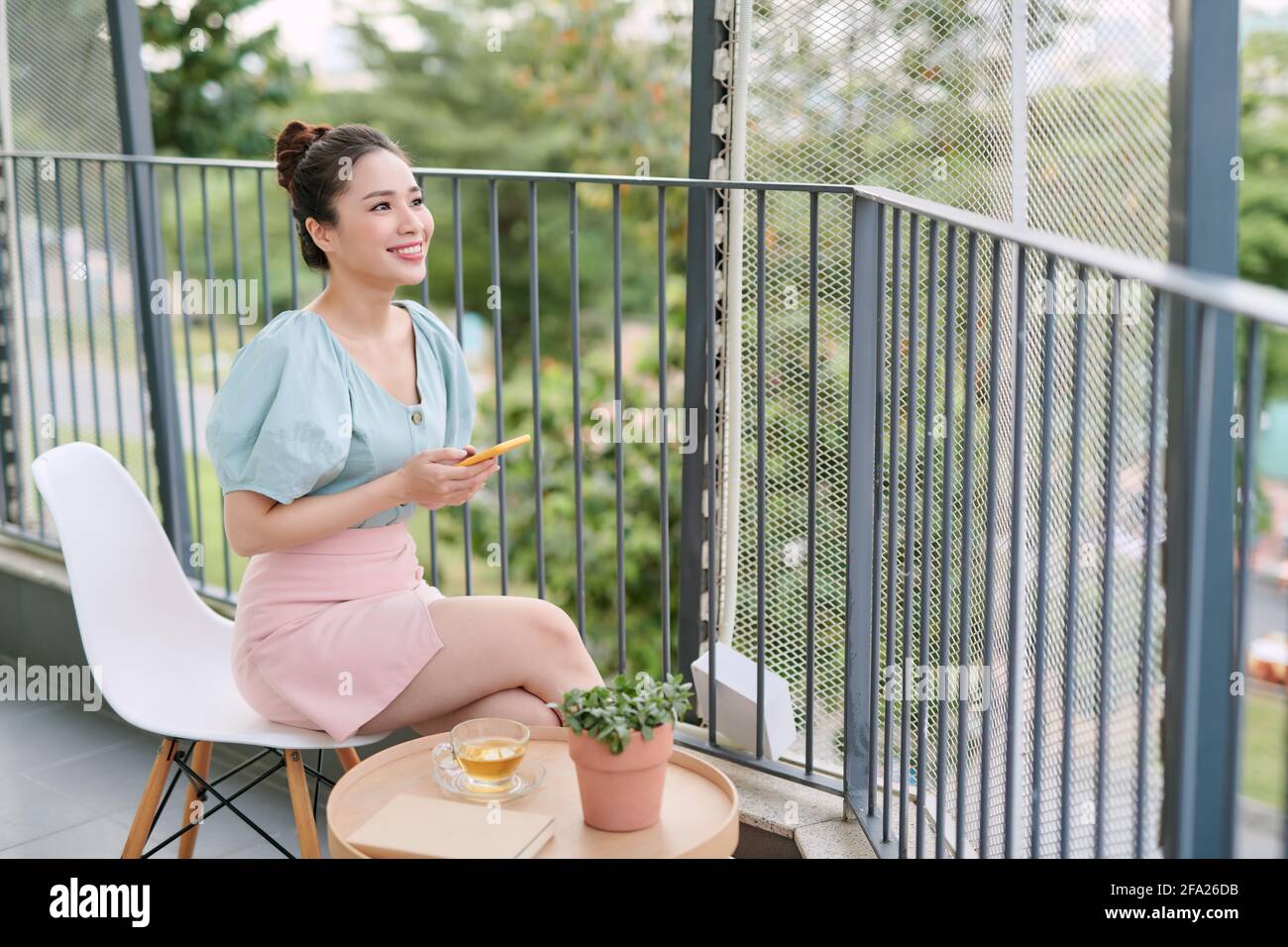 Bella ragazza che ha fatto colazione nel balcone, mentre usa il suo telefono. Foto Stock