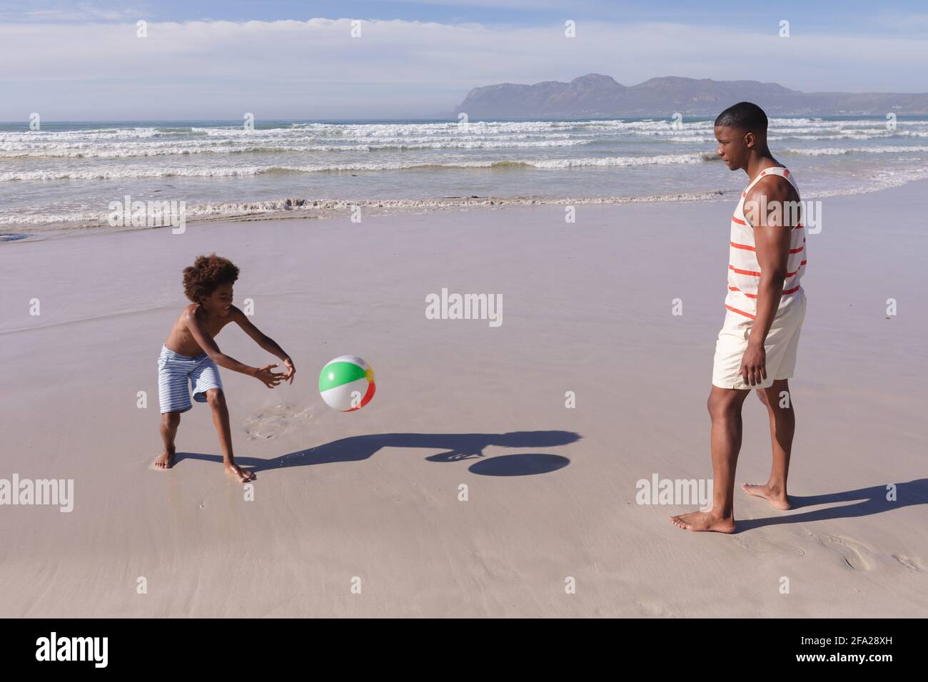 Padre e figlio afro-americano che si divertono a giocare con la palla in spiaggia Foto Stock