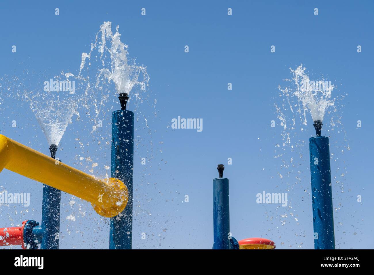 Divertimento estivo per i bambini al paraspruzzi per giocare con l'acqua che cade dalle fontane dai colori luminosi al cielo blu. Foto Stock