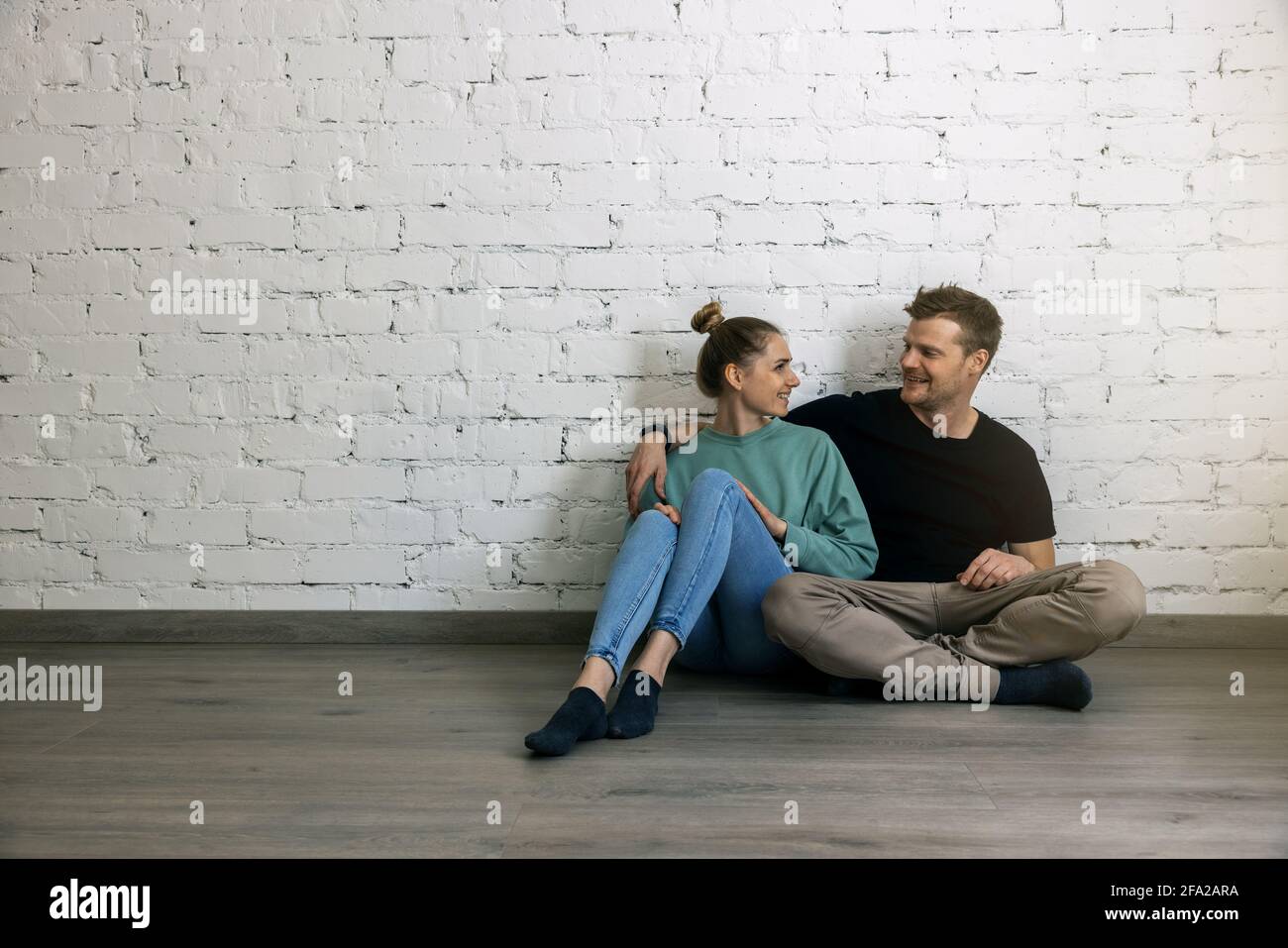 giovane coppia felice seduta sul pavimento accanto alla parete in camera vuota. passaggio a un nuovo concetto di casa. copia spazio Foto Stock