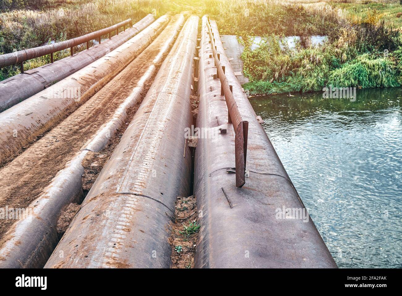 Ponte vuoto composto da vecchi tubi in metallo con ringhiera piccola sul fiume tranquillo in località rurale in bella serata estiva chiudi vista Foto Stock