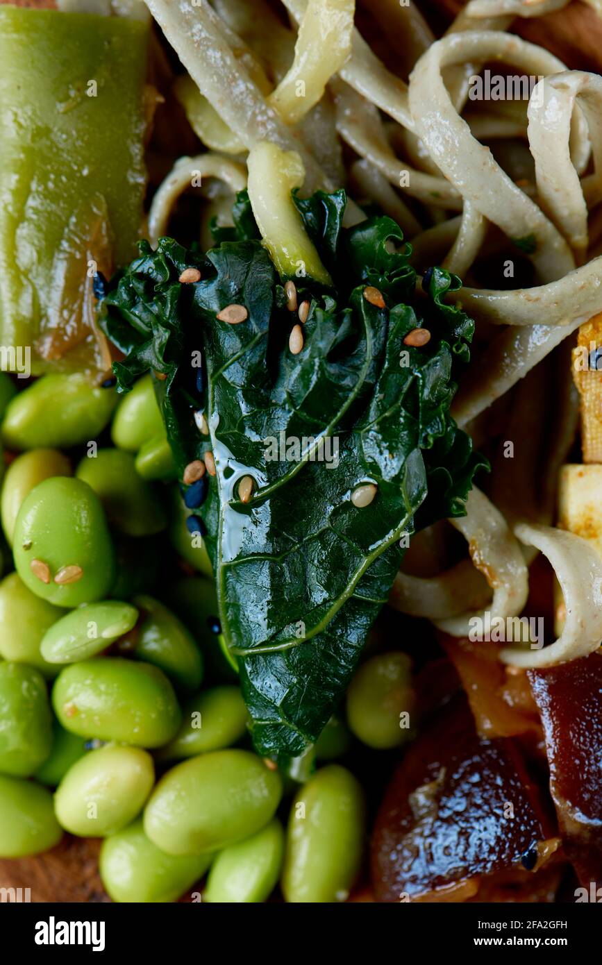 vista ad alto angolo di un piatto di legno con alcune tagliatelle di farro, kale, fagioli di edamame, tofu e funghi shiitake Foto Stock