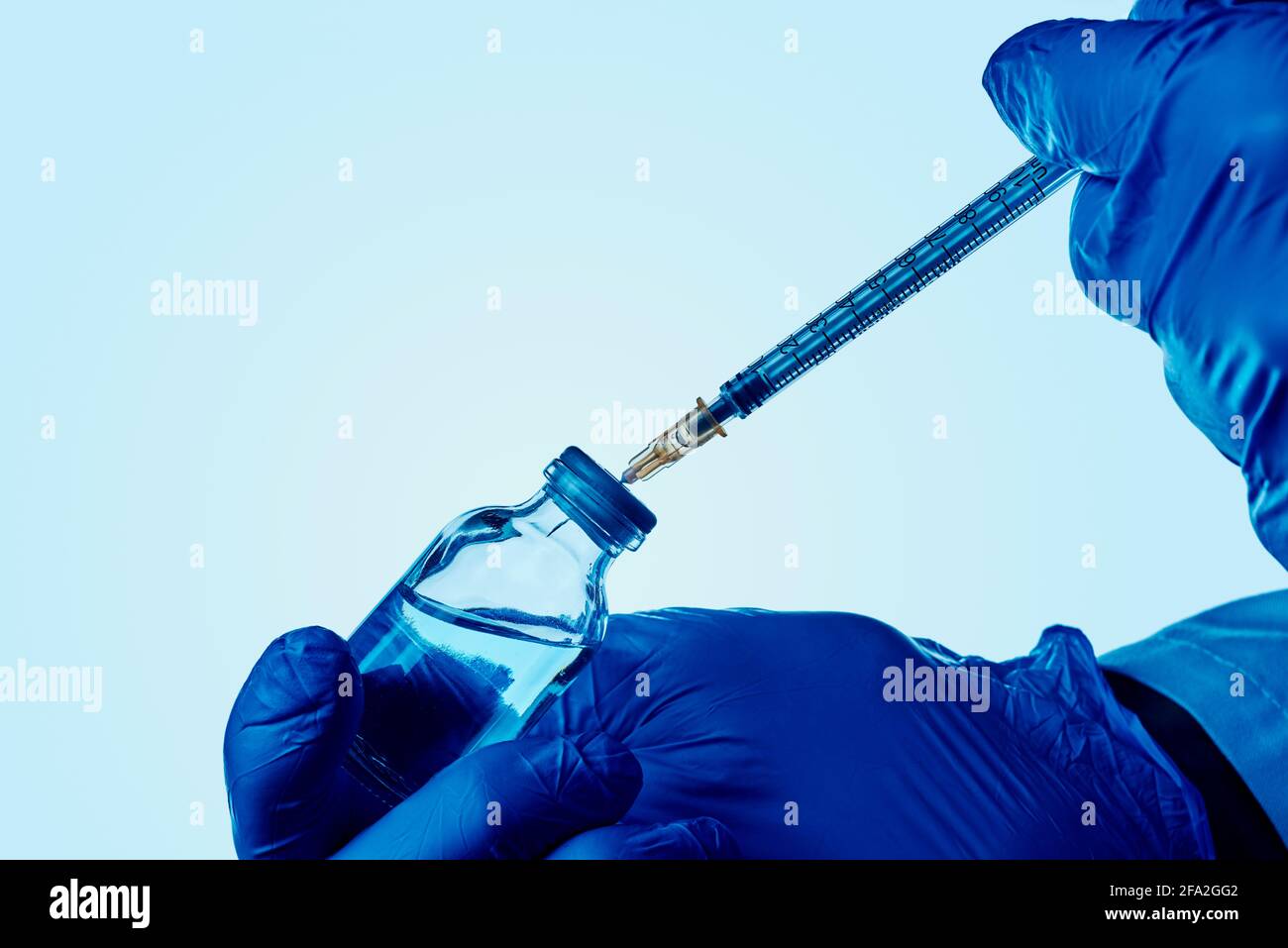 chiusura di un operatore sanitario o di laboratorio, indossando guanti chirurgici blu, riempiendo una siringa di un flaconcino con un liquido blu Foto Stock
