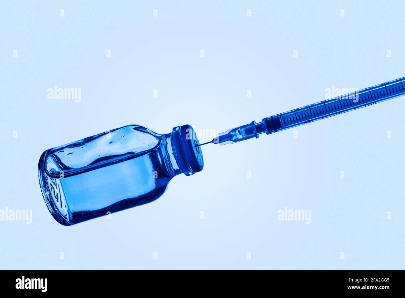chiusura di una siringa in un flaconcino di vaccino con un liquido blu, su sfondo blu chiaro con un po' di spazio vuoto sulla parte superiore Foto Stock