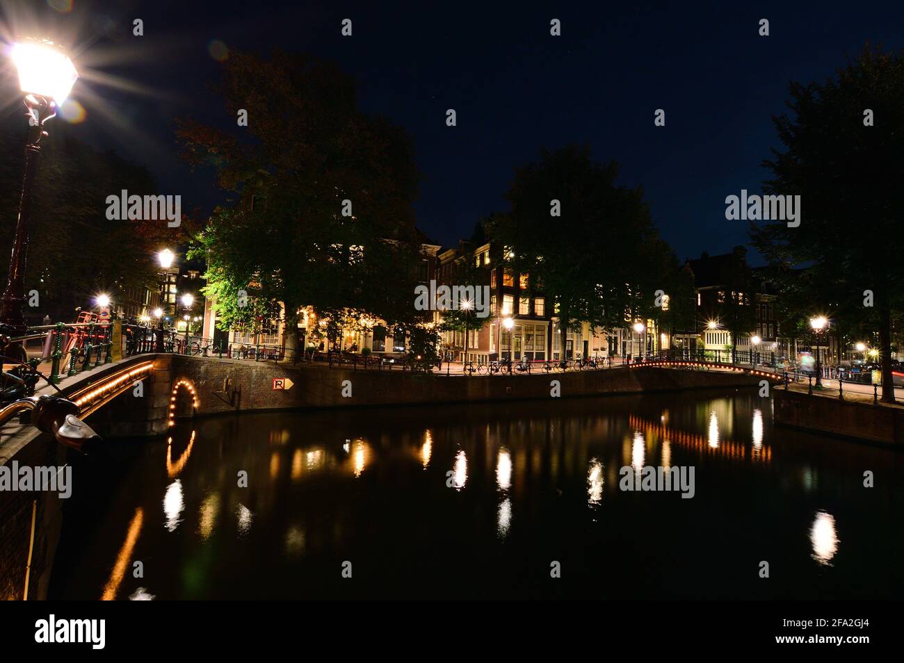 Una notte ad Amsterdam. Il ponte illuminato si riflette nell'acqua del canale. Estate. Foto Stock