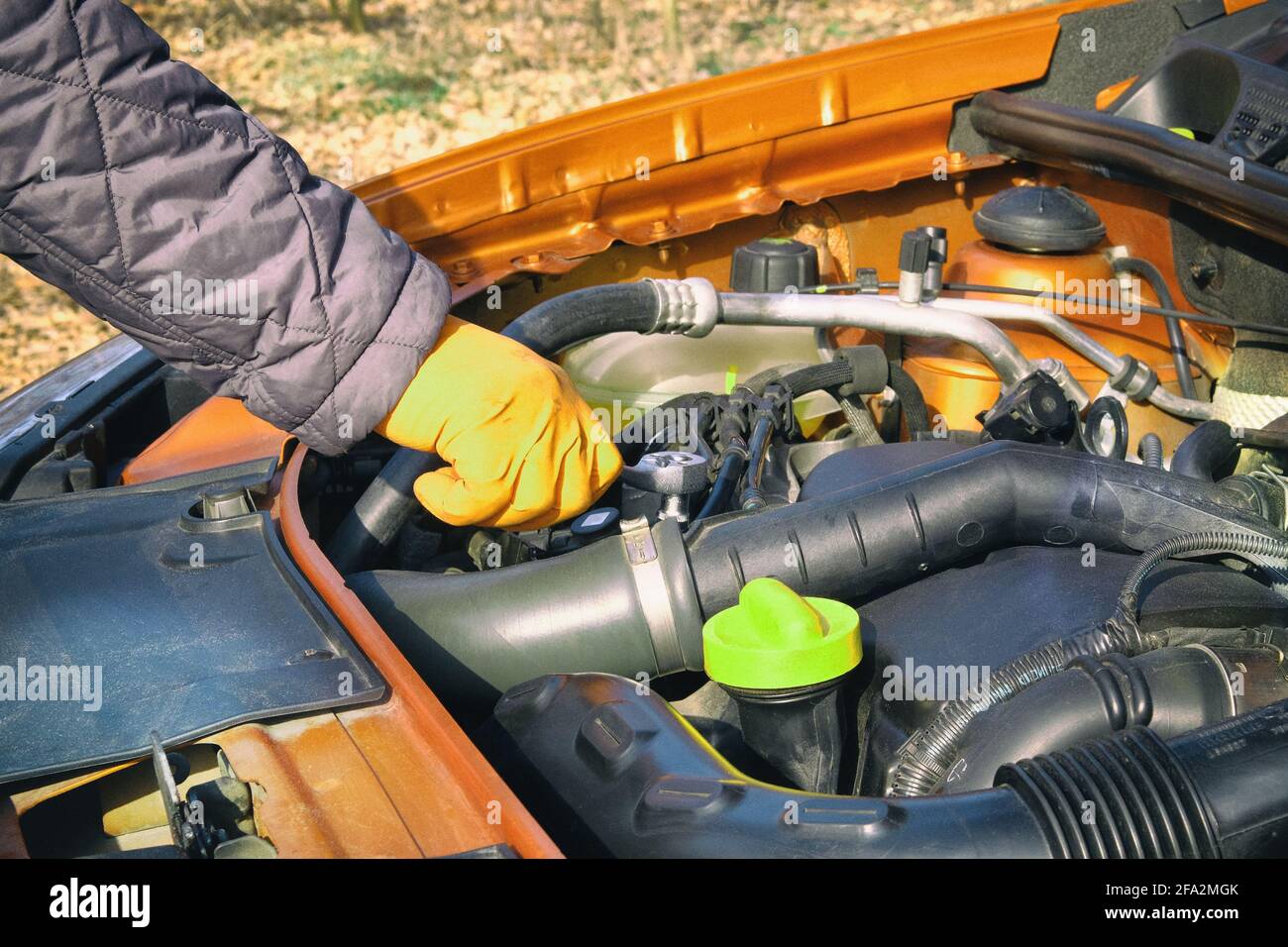 Le mani del conducente in guanti di gomma arancione controllano la vettura, aprire il cofano. Auto e servizio, primo piano. Problemi con la vettura su strada durante la marcia. Foto Stock