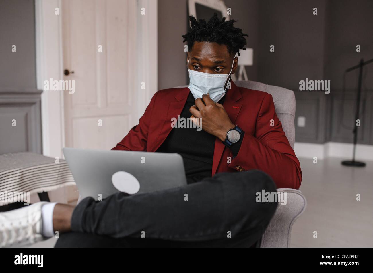 Bell'uomo nero afroamericano che lavora da casa e avere Videochiamata su computer portatile mentre si è seduti su un divano In soggiorno Foto Stock