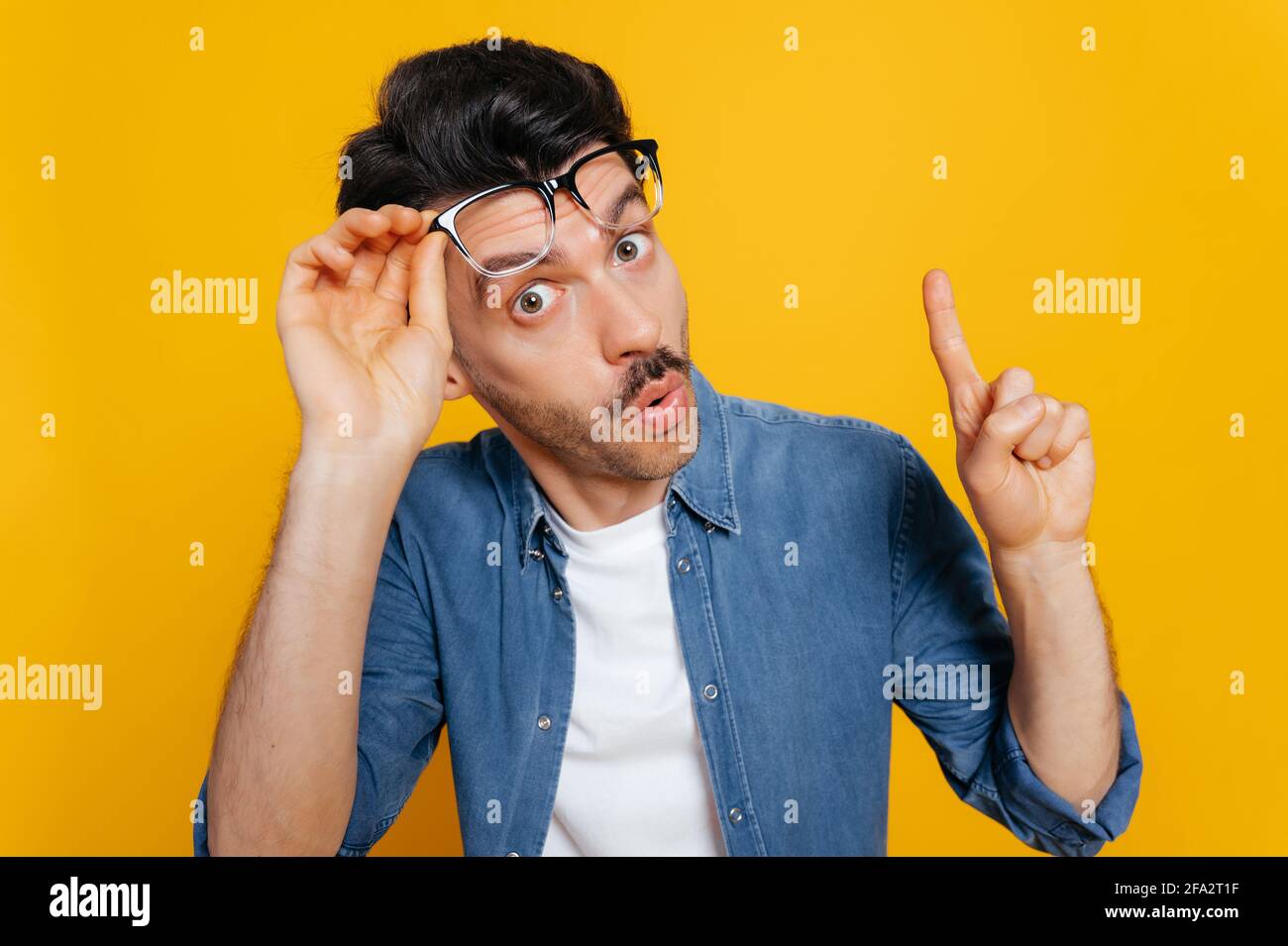 Stupito ragazzo caucasico sorpreso in una t-shirt arancione, scioccato guardando la macchina fotografica con i suoi occhiali sollevati, mostra UN gesto IDEA, in piedi su uno sfondo arancione isolato Foto Stock