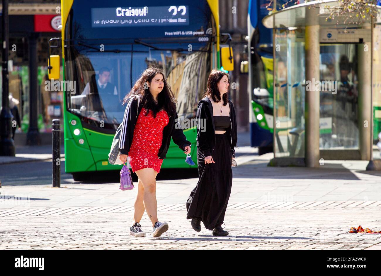 Dundee, Tayside, Scozia, Regno Unito. 22 Apr 2021. Regno Unito Meteo: Un caldo pomeriggio di sole primaverile attraverso la Scozia nord-orientale con temperature che raggiungono i 15°C. Il blocco di Covid-19 si sta allentando con la gente che si riunisce nel centro della città di Dundee con i negozi essenziali ancora aperti per gli affari. Due giovani donne alla moda stanno approfittando delle nuove e rilassanti regole di blocco e del sole tempo di aprile camminando insieme lungo High Street dopo una giornata di shopping. Credit: Dundee Photographics/Alamy Live News Foto Stock
