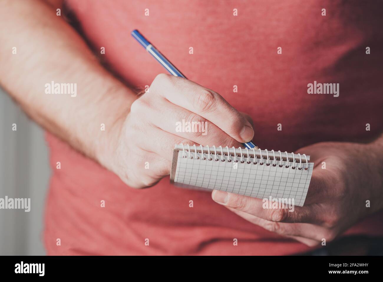 primo piano di uomo che prende appunti su piccolo blocco note a spirale usando una matita Foto Stock
