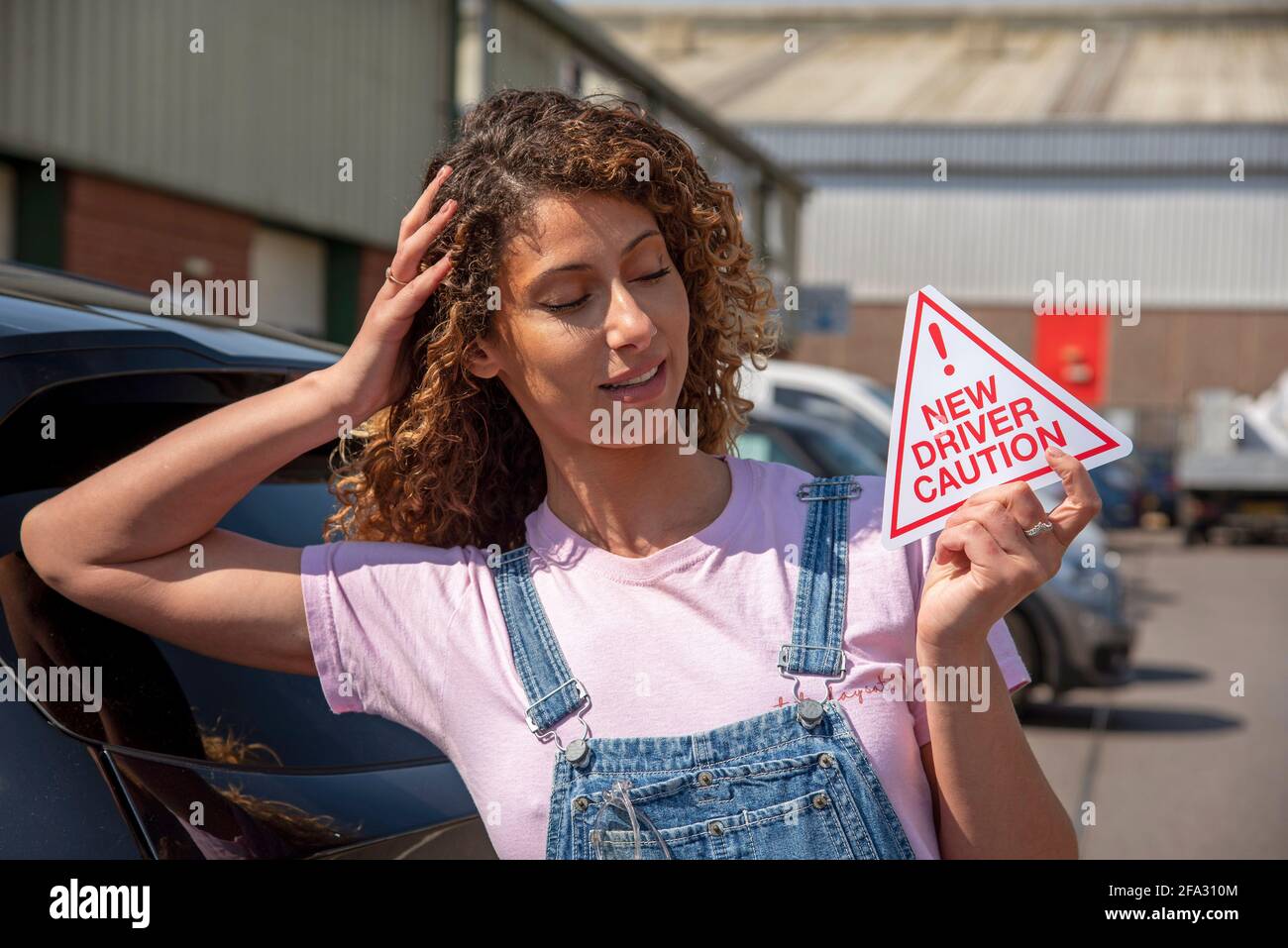 Inghilterra, Regno Unito. 2021. Nuovo pilota, giovane donna attraente che tiene un nuovo segnale di attenzione del conducente da mostrare sulla sua vettura dopo aver superato il test di guida. Foto Stock