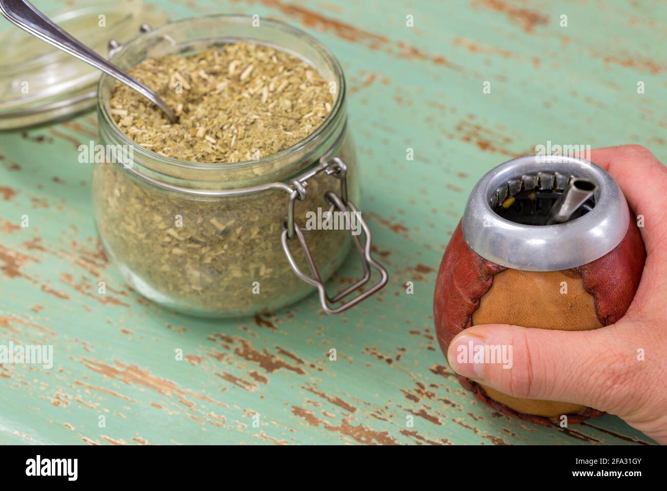 Una mano che tiene un tradizionale vaso di Yerba mate, accanto ad un vaso pieno di vacanze paraguaiane usato per preparare la bevanda Foto Stock