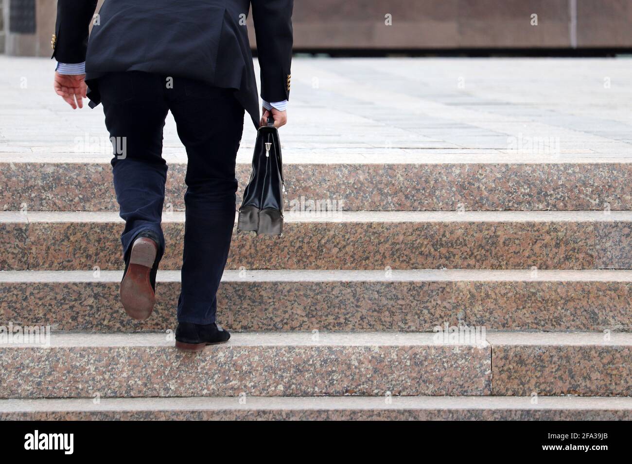 Uomo in tuta da lavoro con valigia che sale scale ripide, gambe maschili in movimento sui gradini. Concetto di carriera, successo, spostamento in alto, ufficiale Foto Stock