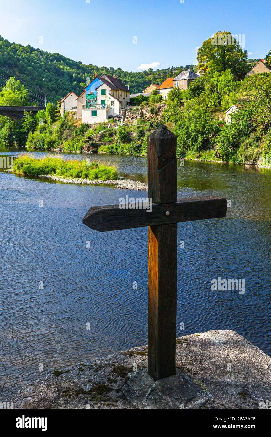 Il borgo medievale di Menat sul fiume Sioule. Sui tralicci del ponte una croce di legno domina il paese. Foto Stock
