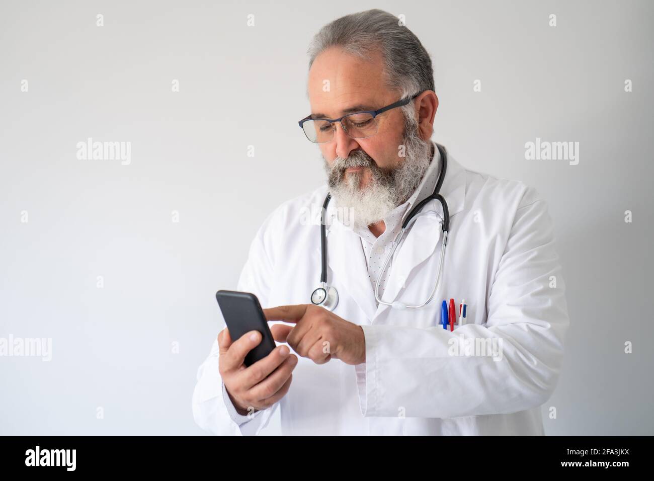 Medico anziano in mano bianca lavorando con il suo smartphone su sfondo bianco. Foto Stock