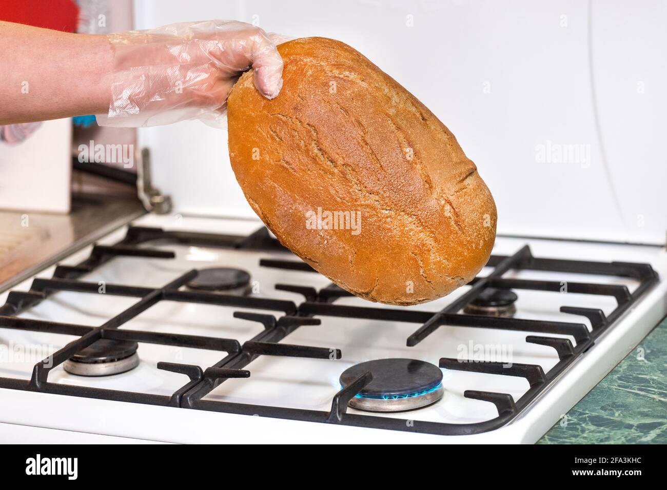 Mano donna in sacchetto di plastica tenere il pane su una stufa a gas, combattendo diversi tipi di batteri e germi a casa. Foto Stock