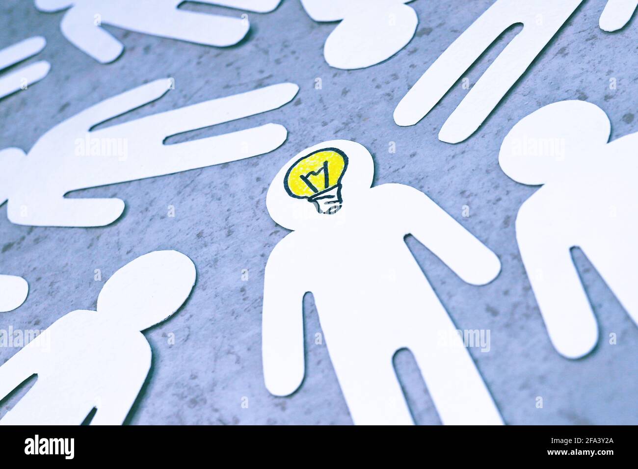 Figure scolpite di persone su sfondo grigio. Lampadina gialla invece di cervello. Persona intelligente nella società, talento, capacità di generare idee. Foto Stock