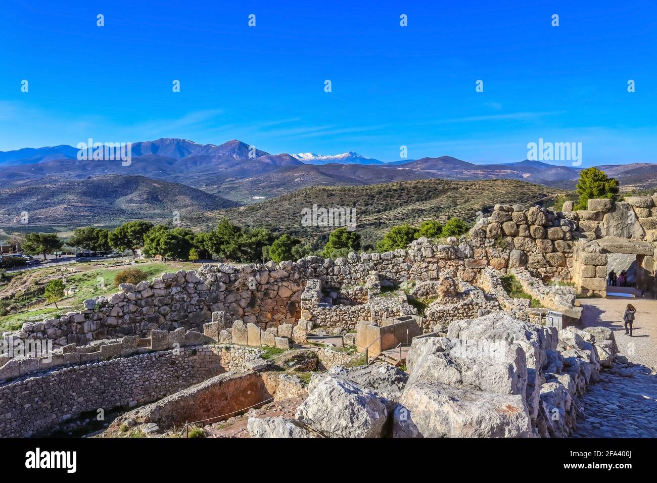 Vista sulle montagne e sulle valli ricche di uliveti Della penisola del Peloponneso dalle rovine collinari di antica Micene con turisti che prendono Foto Stock