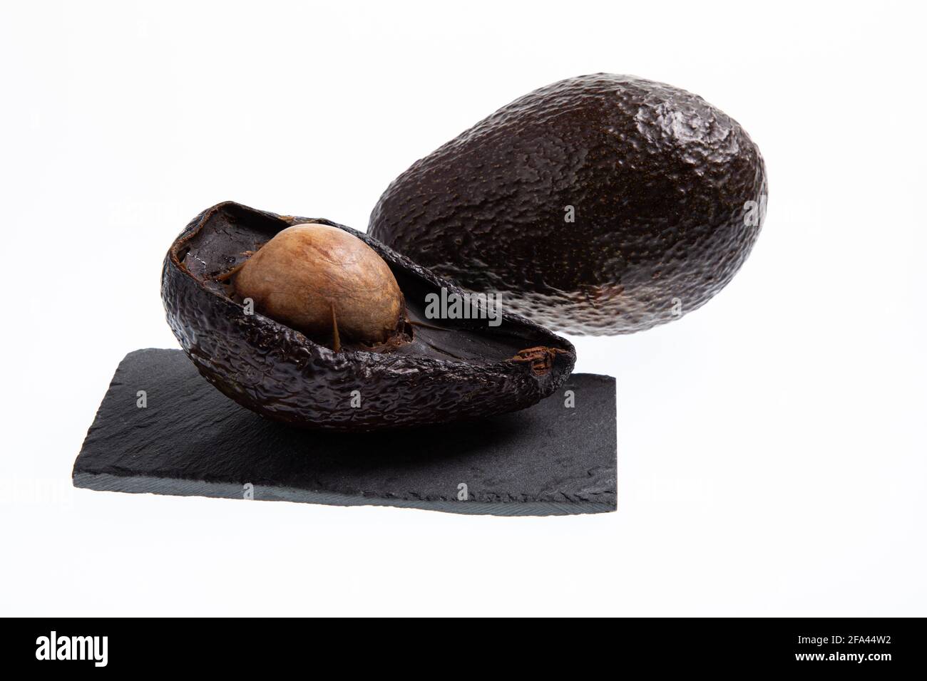 Avocado fresco e maturo accanto all'avocado marcio tagliato in metà con seme visibile isolato su bianco Foto Stock