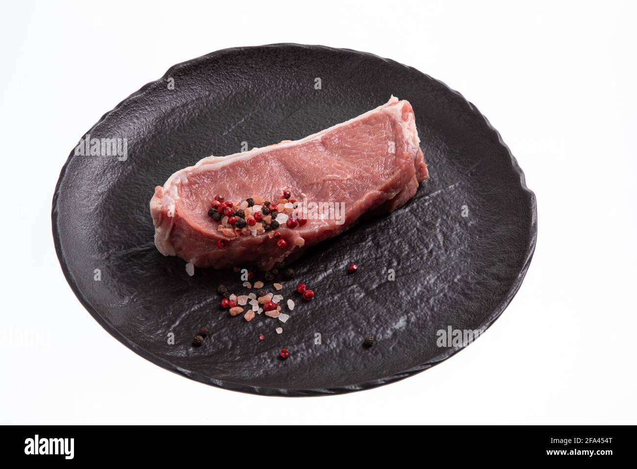 Affettato carne di vitello cruda con un sottile strato di grasso intorno ad essa, pepe rosa e nero e sale marino placcato su piastra di ceramica nera fatta a mano Foto Stock