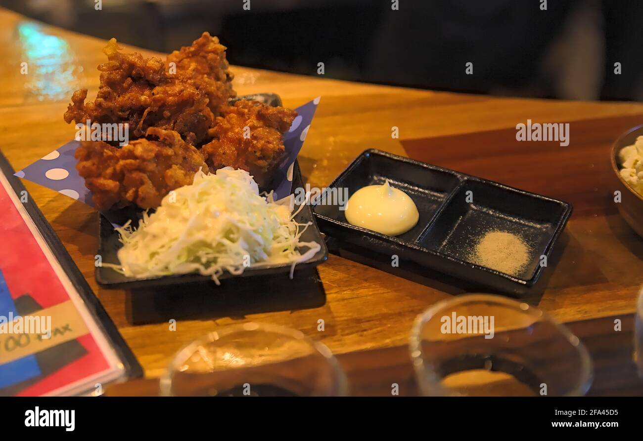 Un piccolo piatto di 'karaage' Giapponese (una specie di pollo fritto) e insalata di contorno servita con maionese e pepe bianco un bancone di legno Foto Stock