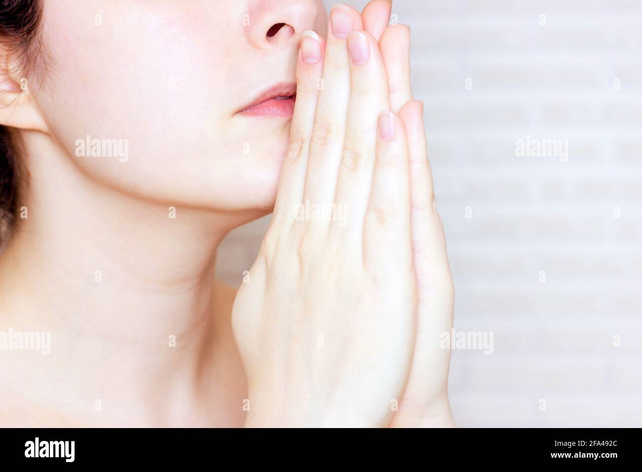 La giovane donna caucasica prega Dio e chiede aiuto con le mani vicino al suo viso. Foto Stock