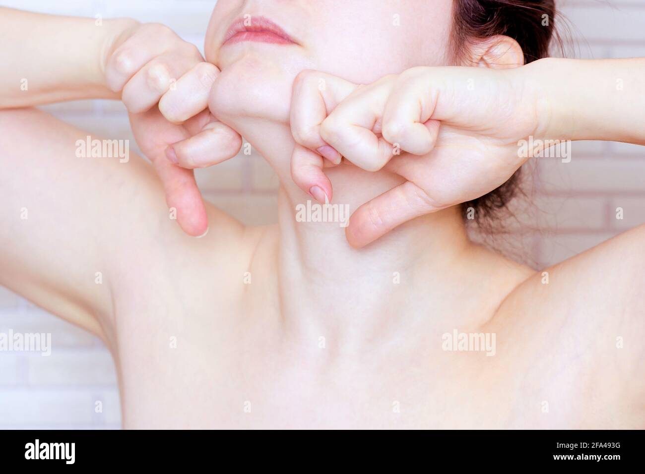 Giovane donna caucasica che tocca il viso con le mani facendo esercizi di fitness viso. Concetto di massaggio e sollevamento del viso. Foto Stock