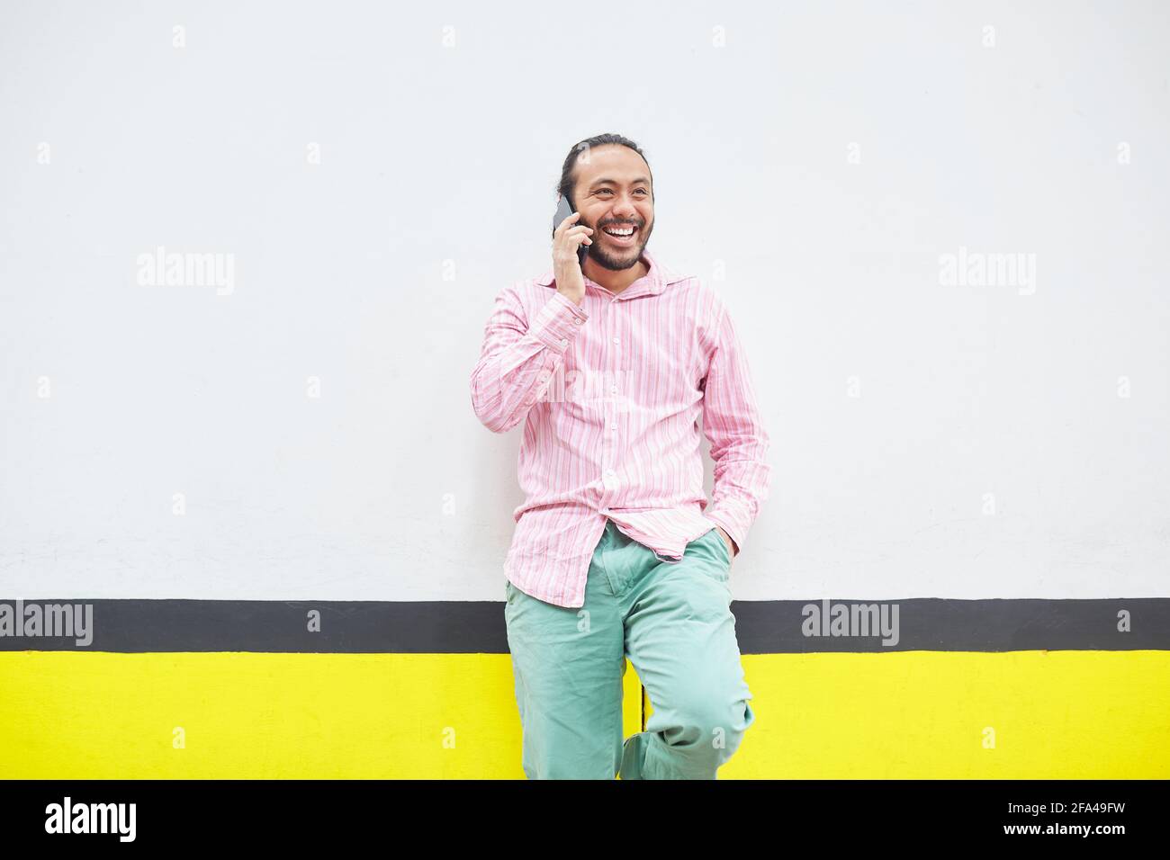 Sorridente uomo ispanico che parla al telefono in un colorato via Foto Stock