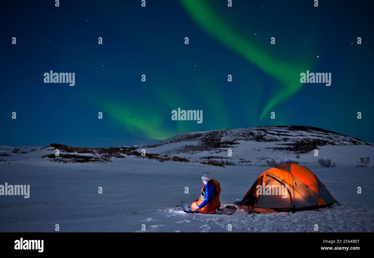 Lo scienziato siede fuori della sua tenda con l'aurora boreale dentro il cielo Foto Stock