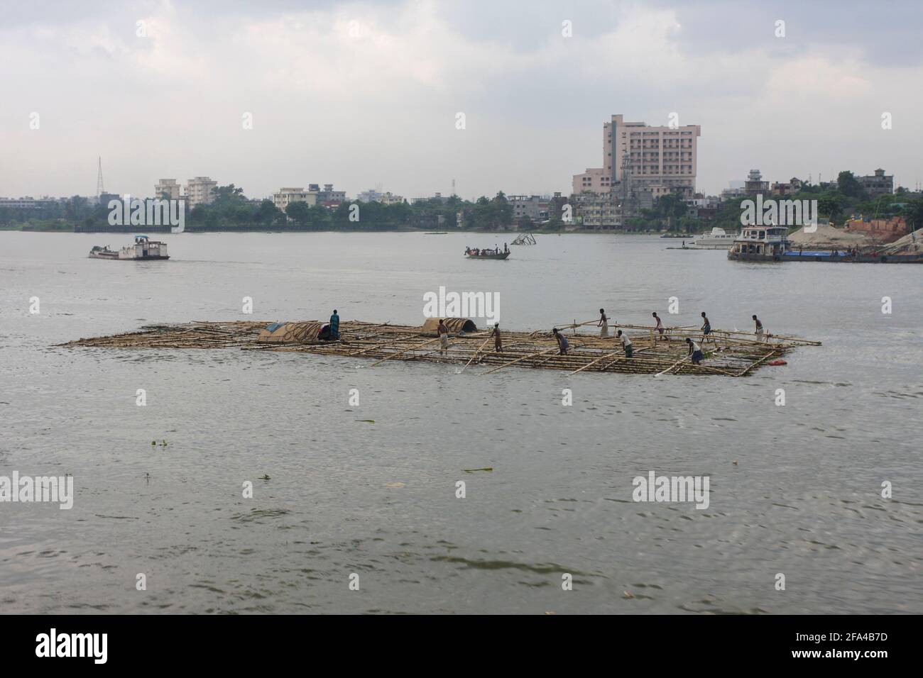 Lavoratori che trasportano bambù che fanno una zattera sul fiume Buriganga, Dhaka, Bangladesh Foto Stock