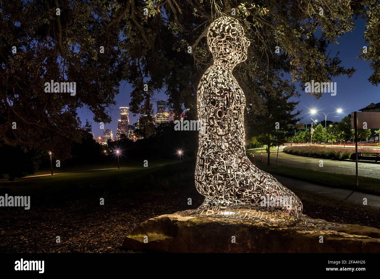 Una delle statue dell'opera d'arte pubblica 'Tolerance' dello scultore spagnolo Jaume Plensa di notte con il centro di Houston, Texas sullo sfondo Foto Stock