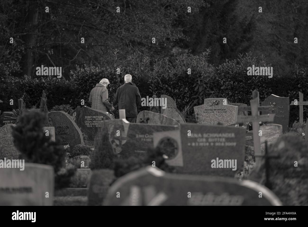 Umkirch, Germania - 24 dicembre 2014: Coppia anziana che rende omaggio di fronte a una tomba in un cimitero dietro una chiesa cattolica. Foto Stock