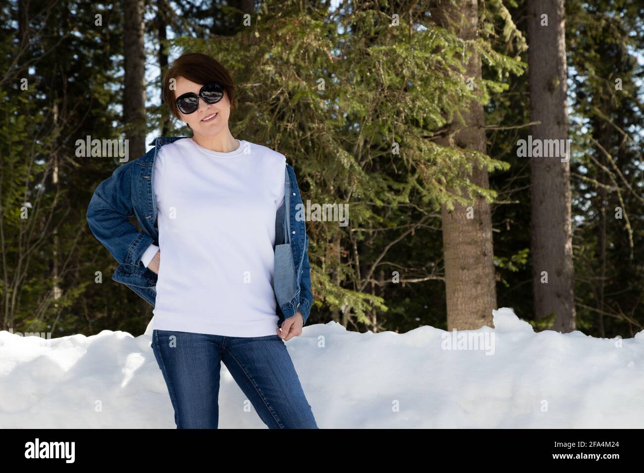 Mockup felpa con collo di cigno in vello bianco con una donna che indossa occhiali da sole in un bosco innevato. Modello felpa pesante, mokup modello Foto Stock