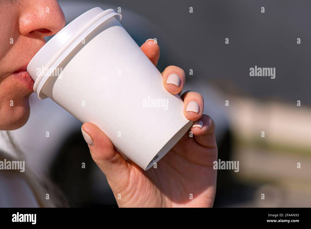 Una donna che tiene una tazza di carta bianca con caffè di bevanda o tè al mattino in una strada della città, tazza bianca di cartone bianco Foto Stock