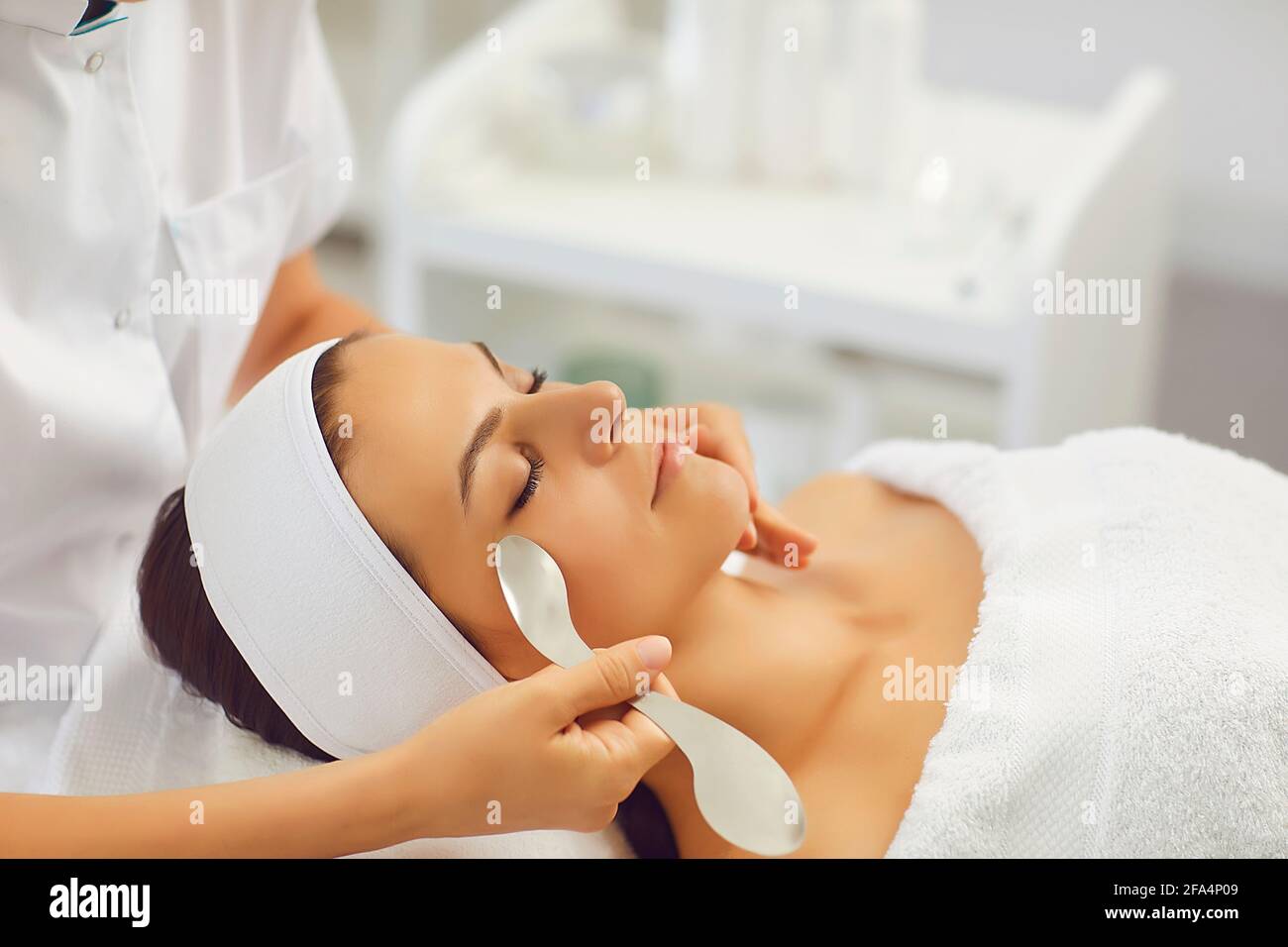 La donna soddisfatta sta con gli occhi chiusi nell'ufficio del massaggiatore e riceve un massaggio facciale. Foto Stock