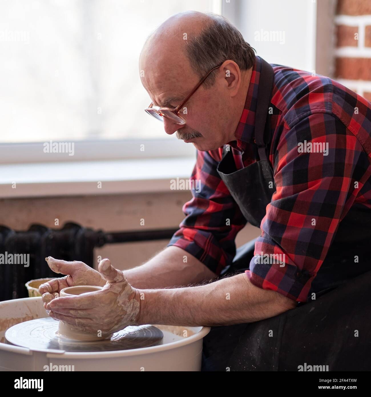 Vasaio maschio anziano che crea la ciotola in laboratorio di ceramica. Hobby alla vecchiaia. Orientamento quadrato Foto Stock